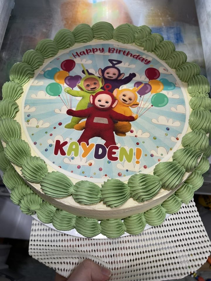 Custom birthday cake featuring a Teletubbies edible print and the name Kayden, decorated with green frosting borders.