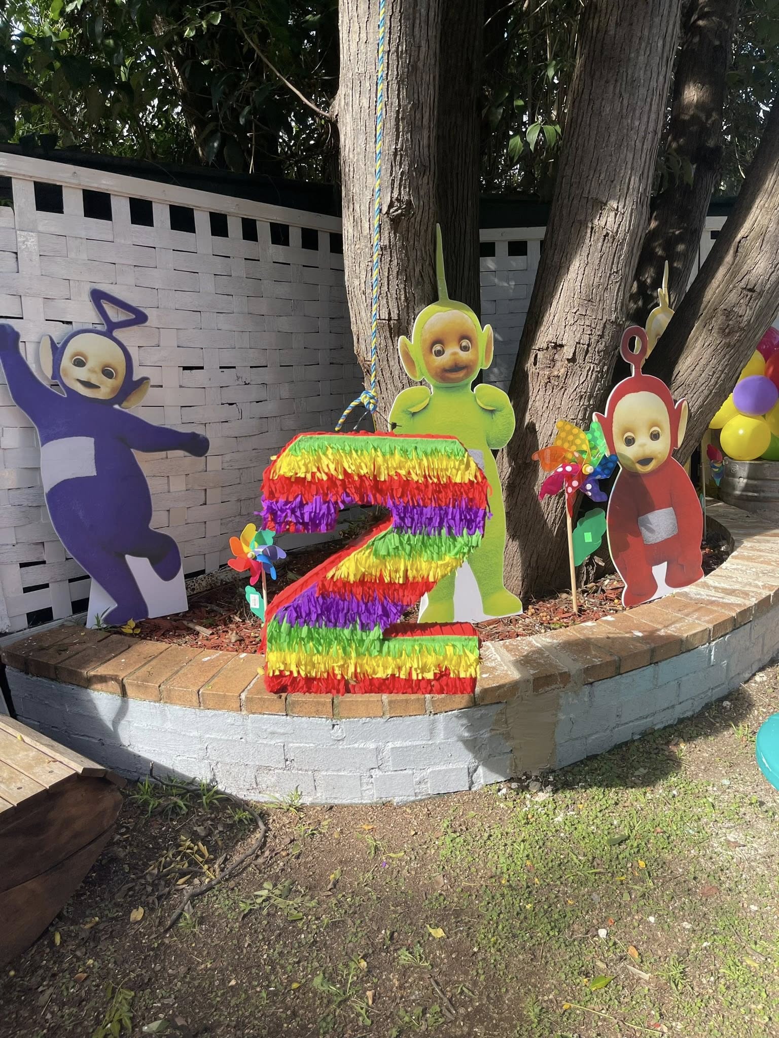 Colorful number two piñata surrounded by Teletubbies party cutouts in a garden setting