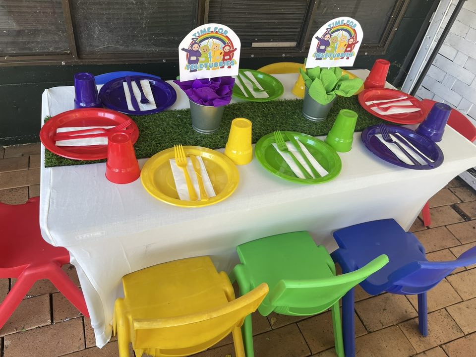 Teletubbies themed children's party table setting with colorful plates, cups, and chairs
