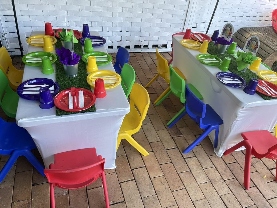 Colorful children's party tables with plastic chairs, vibrant plates, and grass placemats.