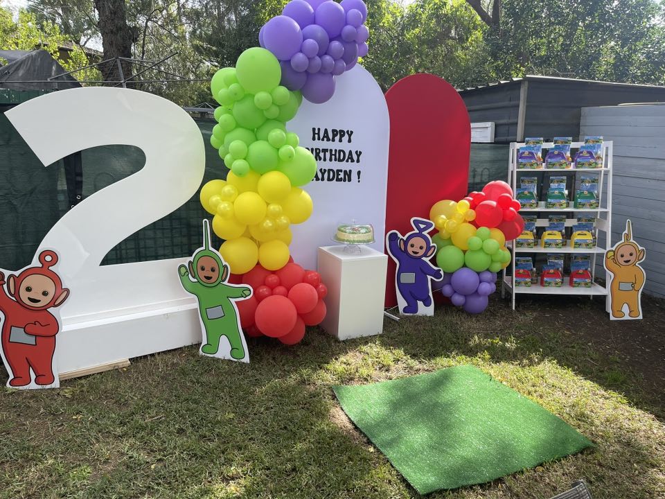 Teletubbies themed 2nd birthday party setup with balloon arches, character cutouts, and party favor display.