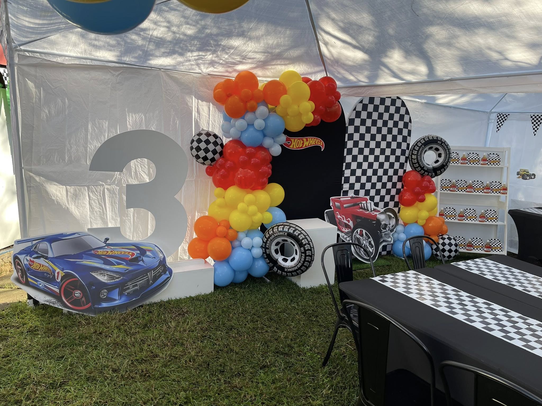 Hot Wheels themed 3rd birthday party setup featuring race car decorations, balloons, and a checkered flag backdrop.