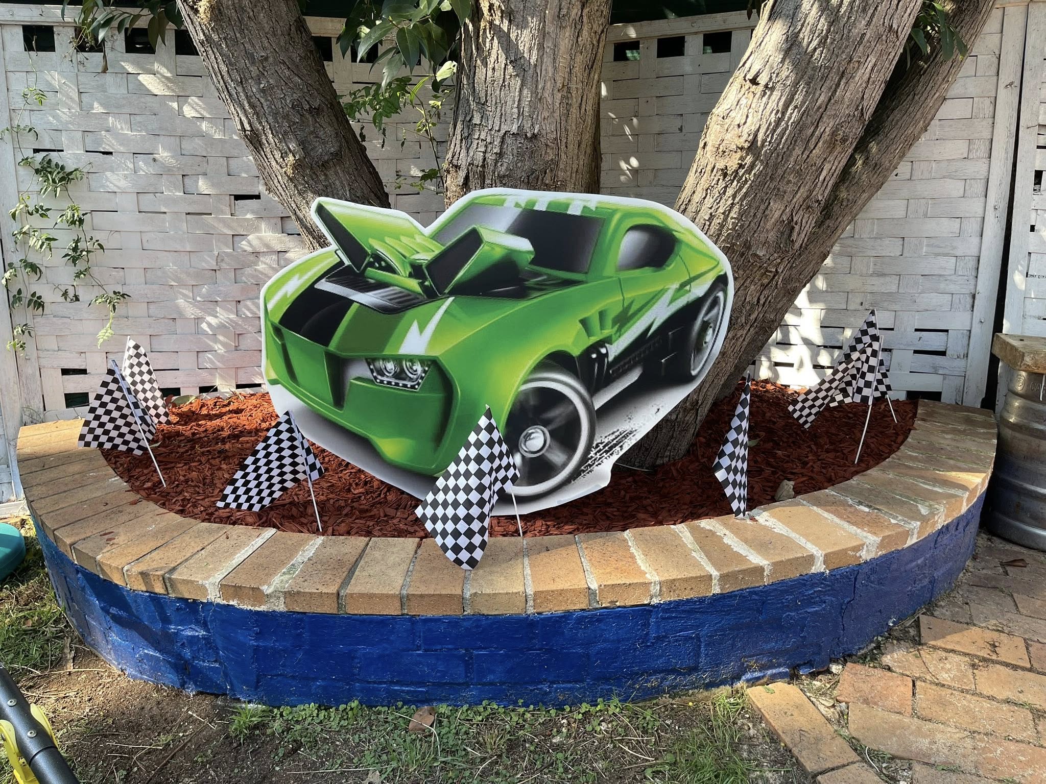 Green toy race car cutout with checkered flags in a garden bed