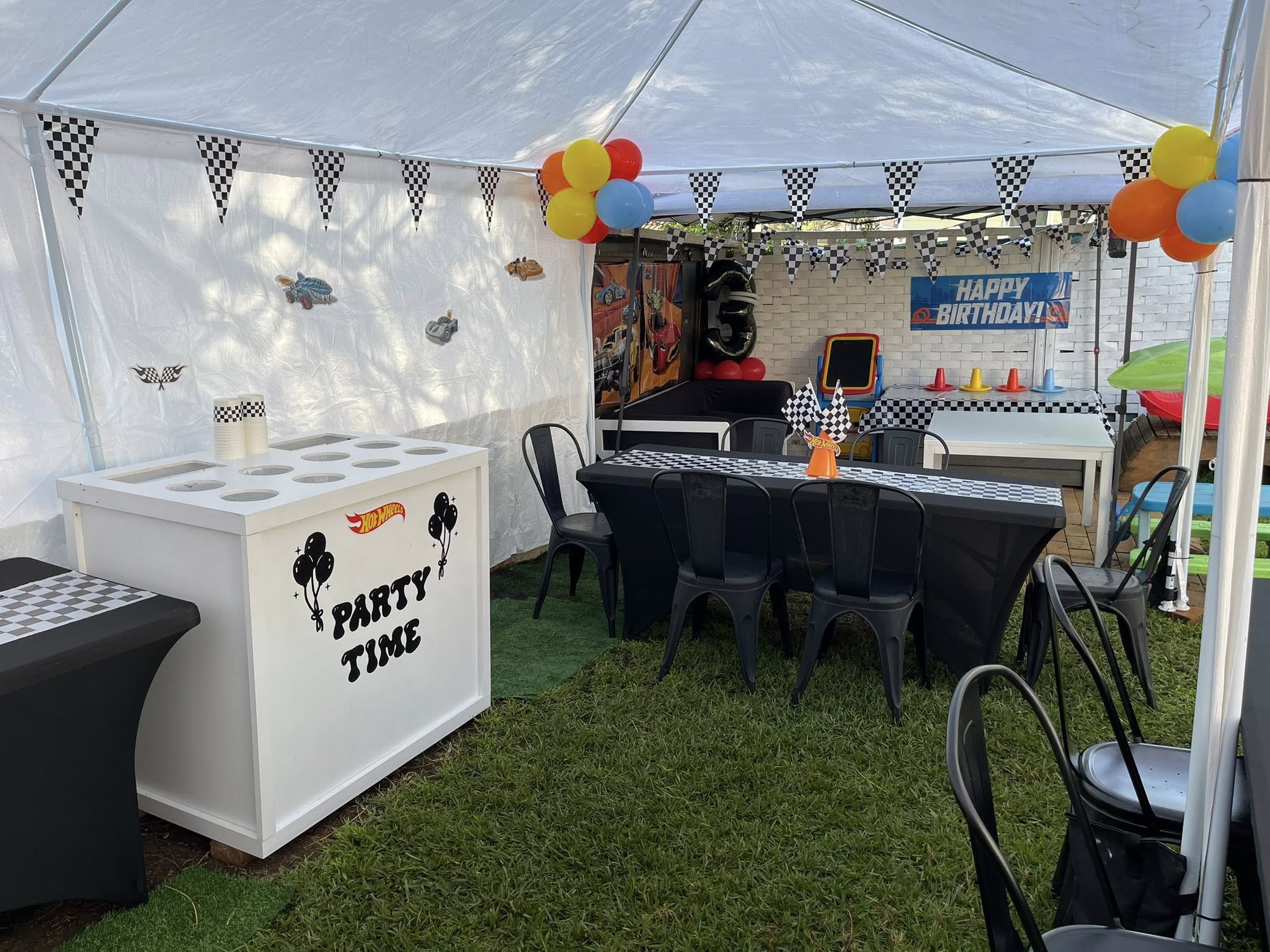 Hot Wheels themed outdoor birthday party setup with black table covers, checkered flags, and party decorations.