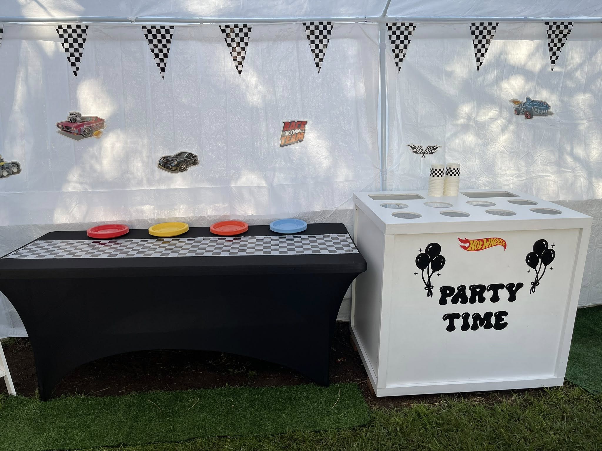 Hot Wheels themed party setup with checkered flag banners, race car wall cutouts, and a Party Time snack station.