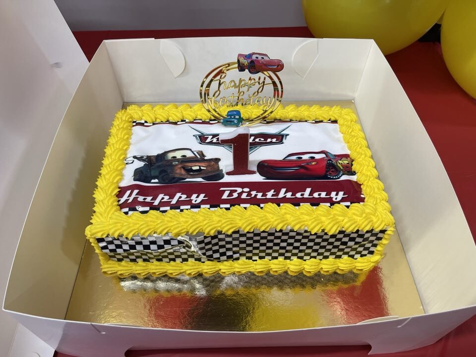 Rectangular Cars-themed birthday cake with yellow frosting and checkered piping.