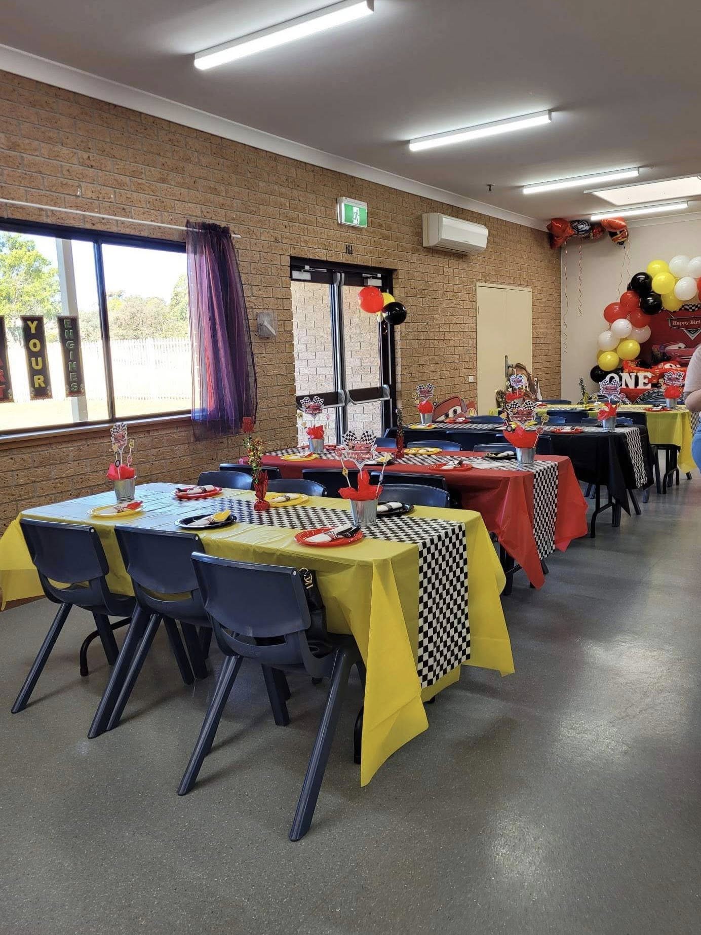 Race car themed party tables with yellow and red tablecloths, black checkerboard runners, and matching centerpieces.