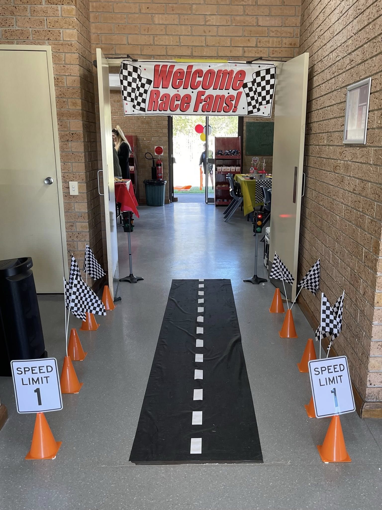 Race car themed party entrance with a Welcome Race Fans banner, road runway, cones, and speed limit signs.