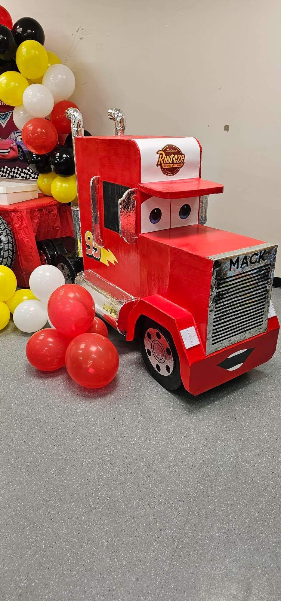 DIY cardboard Mack truck prop from Cars movie surrounded by red, yellow, black, and white balloons