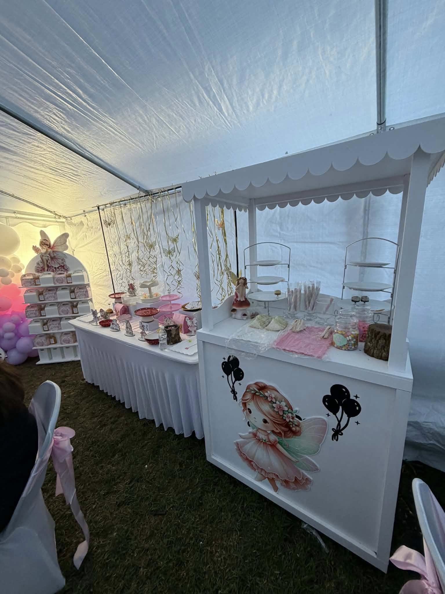 Fairy-themed dessert cart and party table display with pink decorations under a white tent canopy