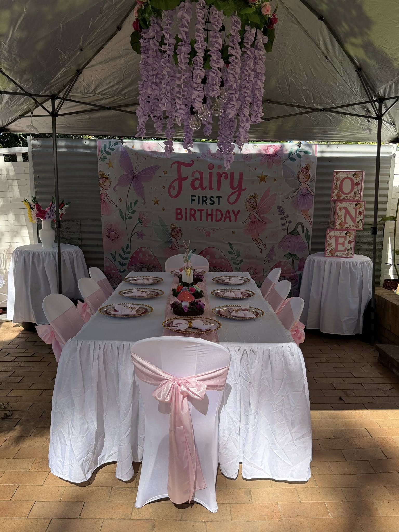 Fairy-themed first birthday party setup with decorated dining table, floral backdrop and ONE block display.