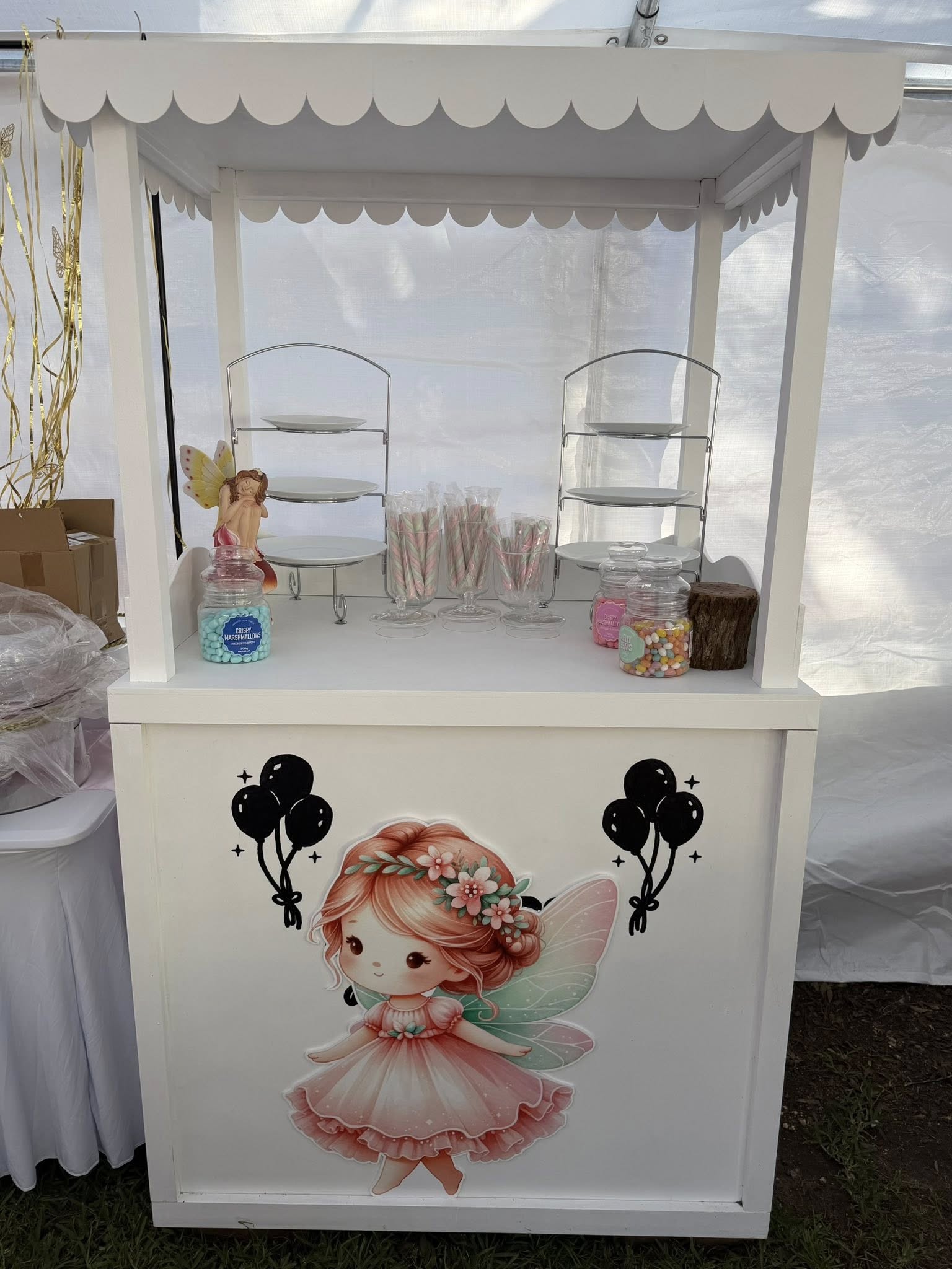 White party snack cart decorated with a fairy illustration and filled with tiers of sweets and candy jars.