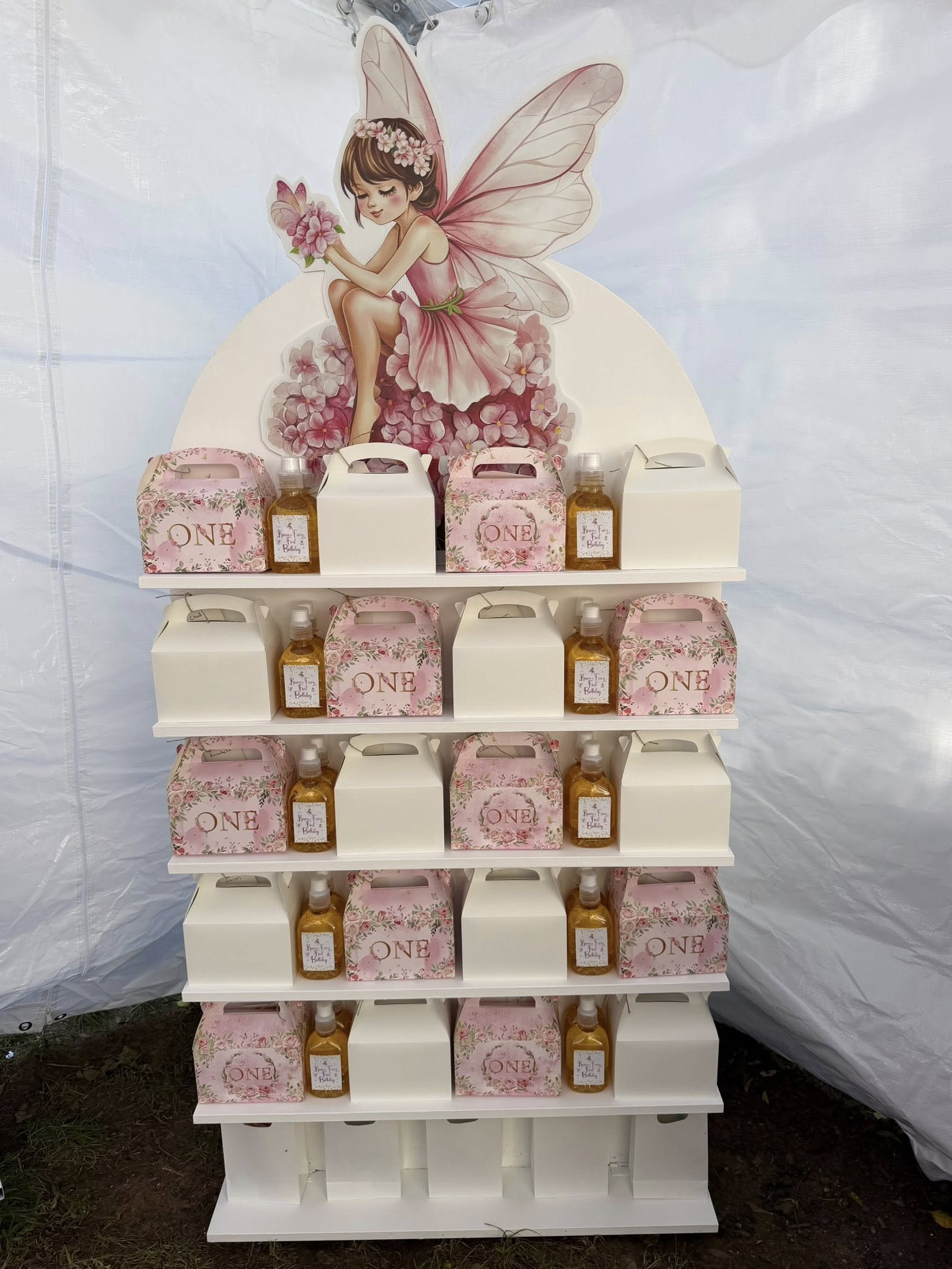 Display rack filled with first birthday party favor boxes and small hand sanitizer bottles featuring a fairy theme.