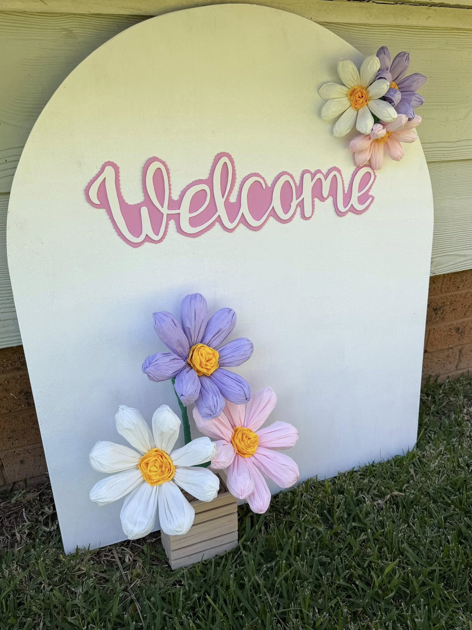 Arched wooden welcome sign decorated with pastel paper flowers