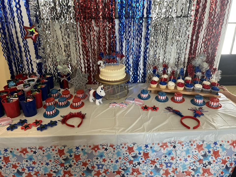 Patriotic themed birthday party table with a cake, cupcakes, and red, white, and blue party favors.