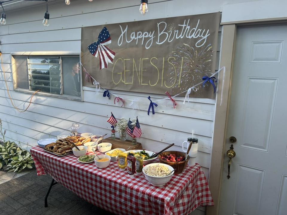 Patriotic themed birthday party food table with a red and white checkered tablecloth and Happy Birthday Genesis banner.