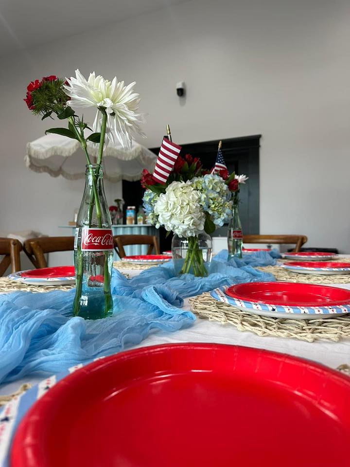 Patriotic table setting with red plates, blue fabric runner, and Coca-Cola bottle vases with flowers
