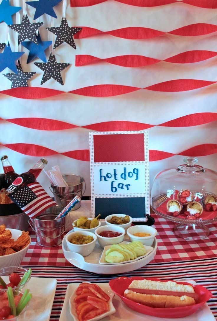 Hot dog bar set up for an American-themed party with condiment bowls, toppings, and red and white decorations.