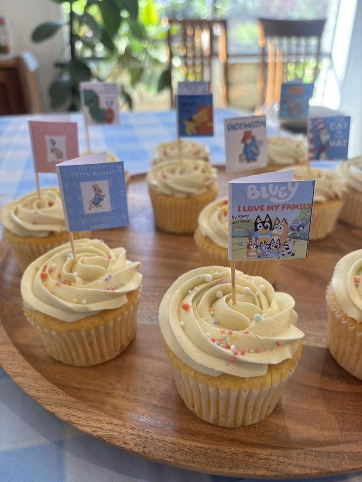 Cupcakes topped with miniature book cover decorations featuring children's titles like Bluey, Peter Rabbit, and Paddington.
