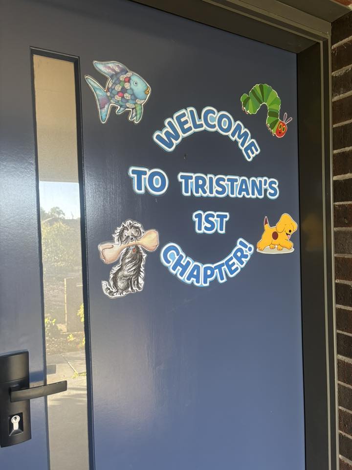 Blue door decorated with children's storybook character stickers and a sign reading Welcome to Tristan's 1st Chapter.