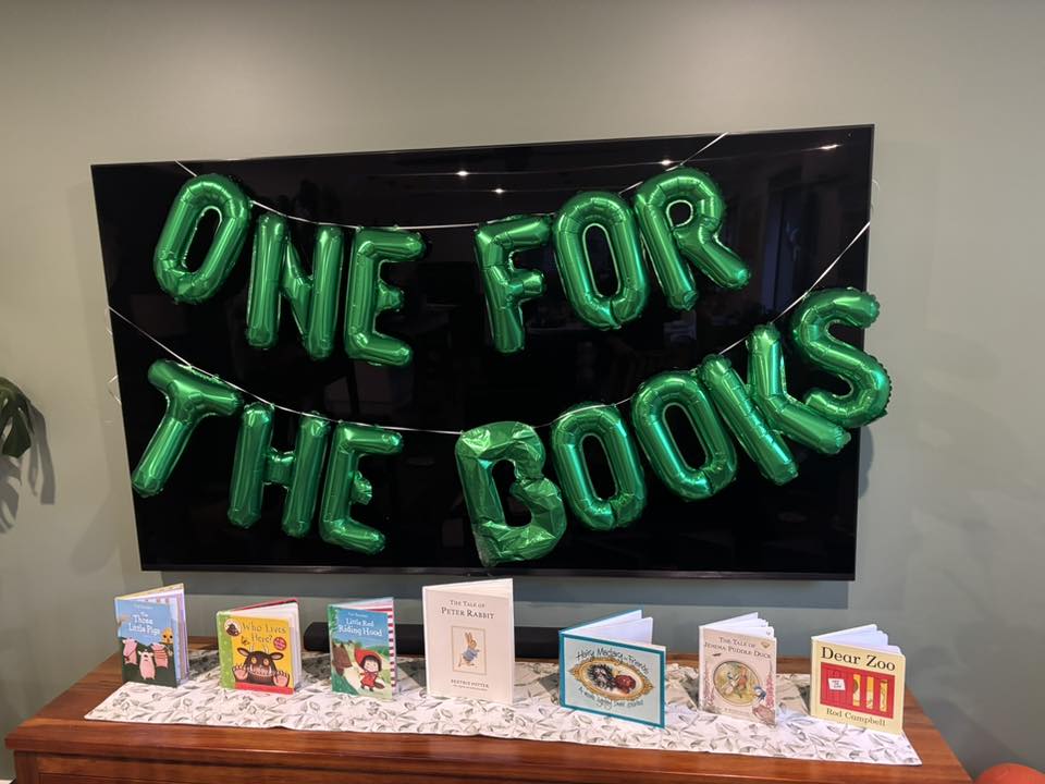 Display featuring classic children's books and green balloon letters reading One For The Books.