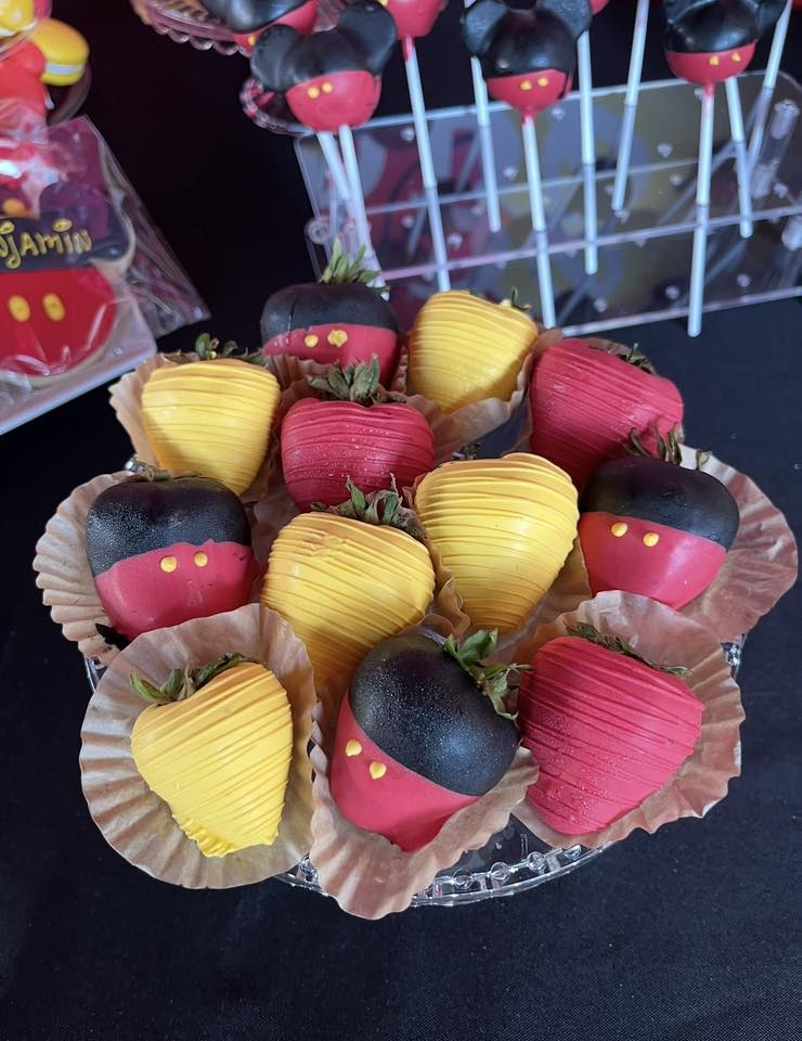 Mickey Mouse themed chocolate covered strawberries in red and yellow designs on a serving tray