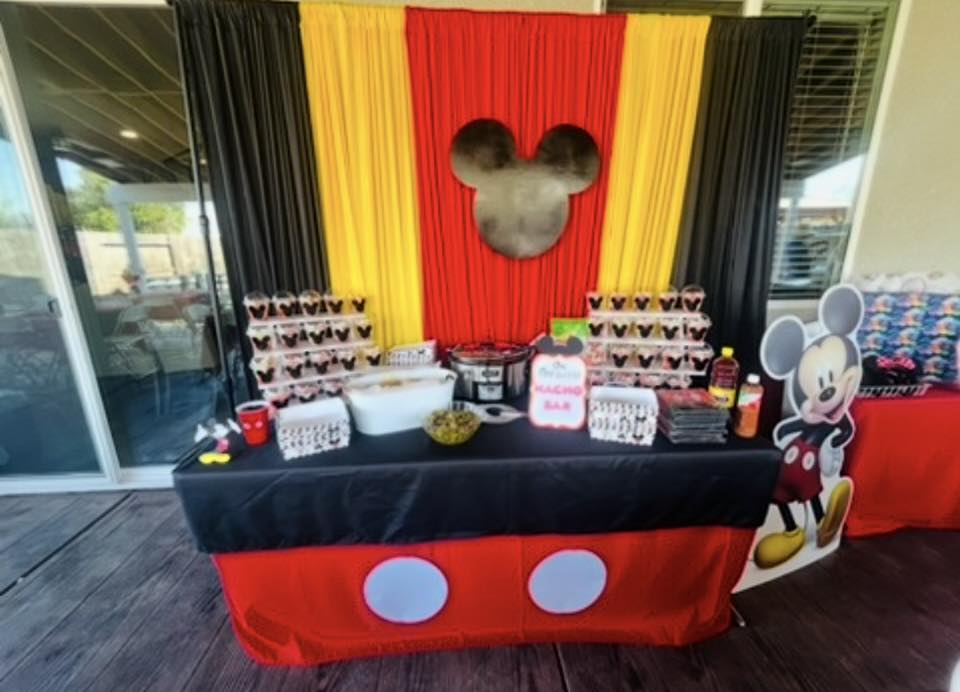 Mickey Mouse themed party food table with a red, yellow, and black draped backdrop.