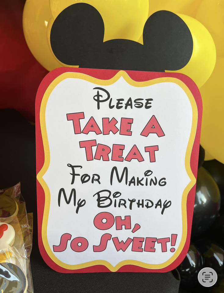 Mickey Mouse shaped sign that says Please Take A Treat For Making My Birthday Oh So Sweet.