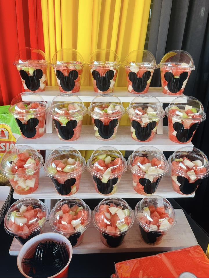 Individual clear dessert cups filled with diced fruit, each featuring a black Mickey Mouse silhouette decal.