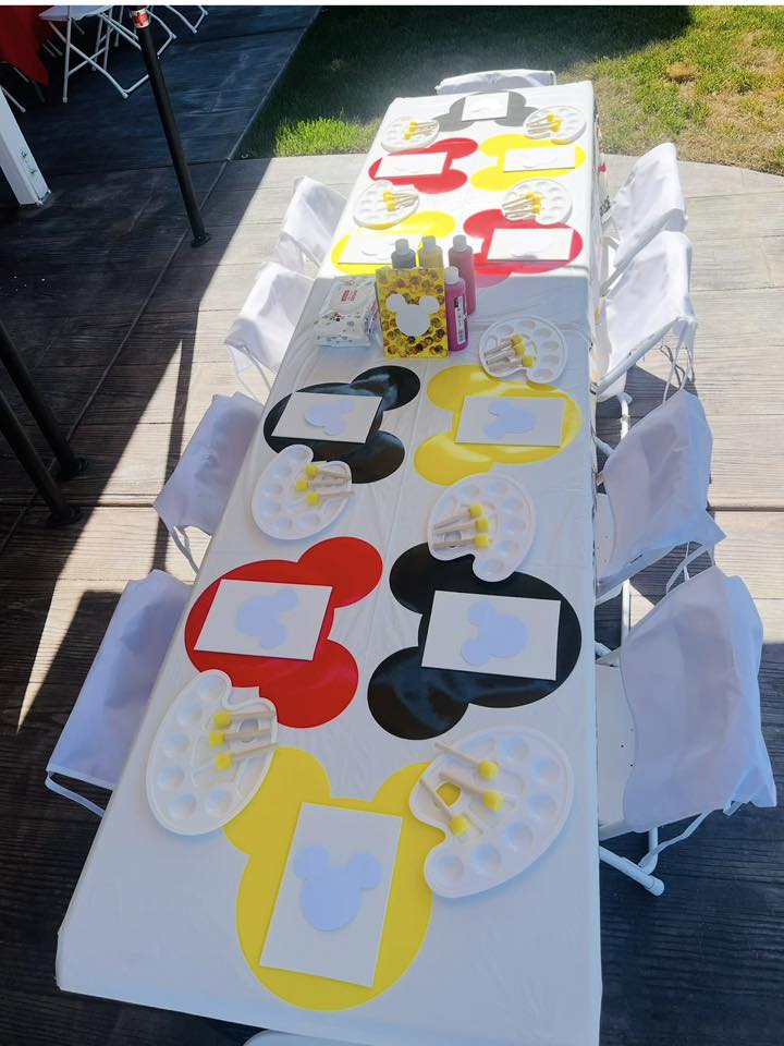 Table set up for a Mickey Mouse themed kids painting party with mouse-shaped placemats and paint palettes.