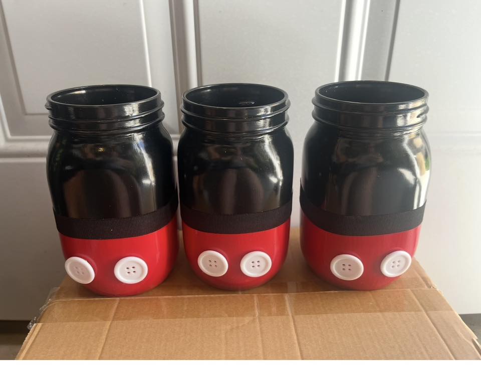 Three painted mason jars themed after Mickey Mouse with black tops, red bottoms, and white button details.