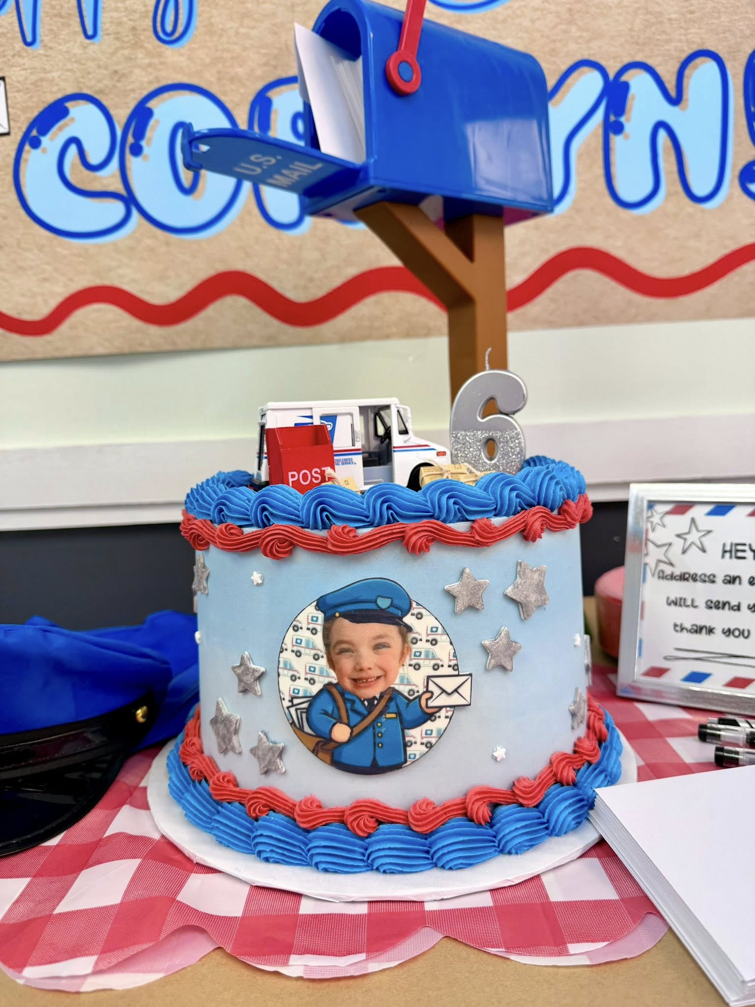 Mail carrier themed birthday cake with a blue mailbox topper and a photo of a child dressed as a mailman