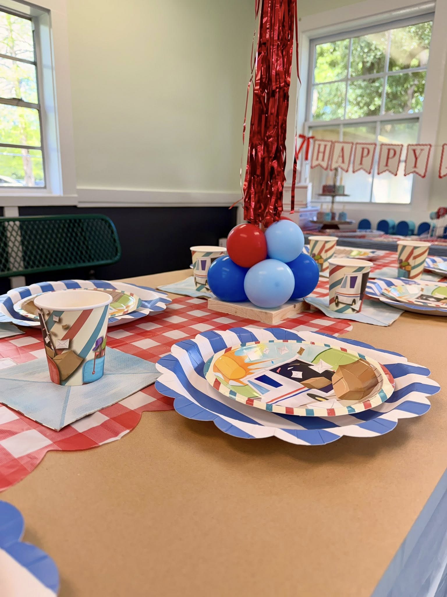 Mail carrier themed party table setting with patterned paper plates, cups, and red, white, and blue balloons.