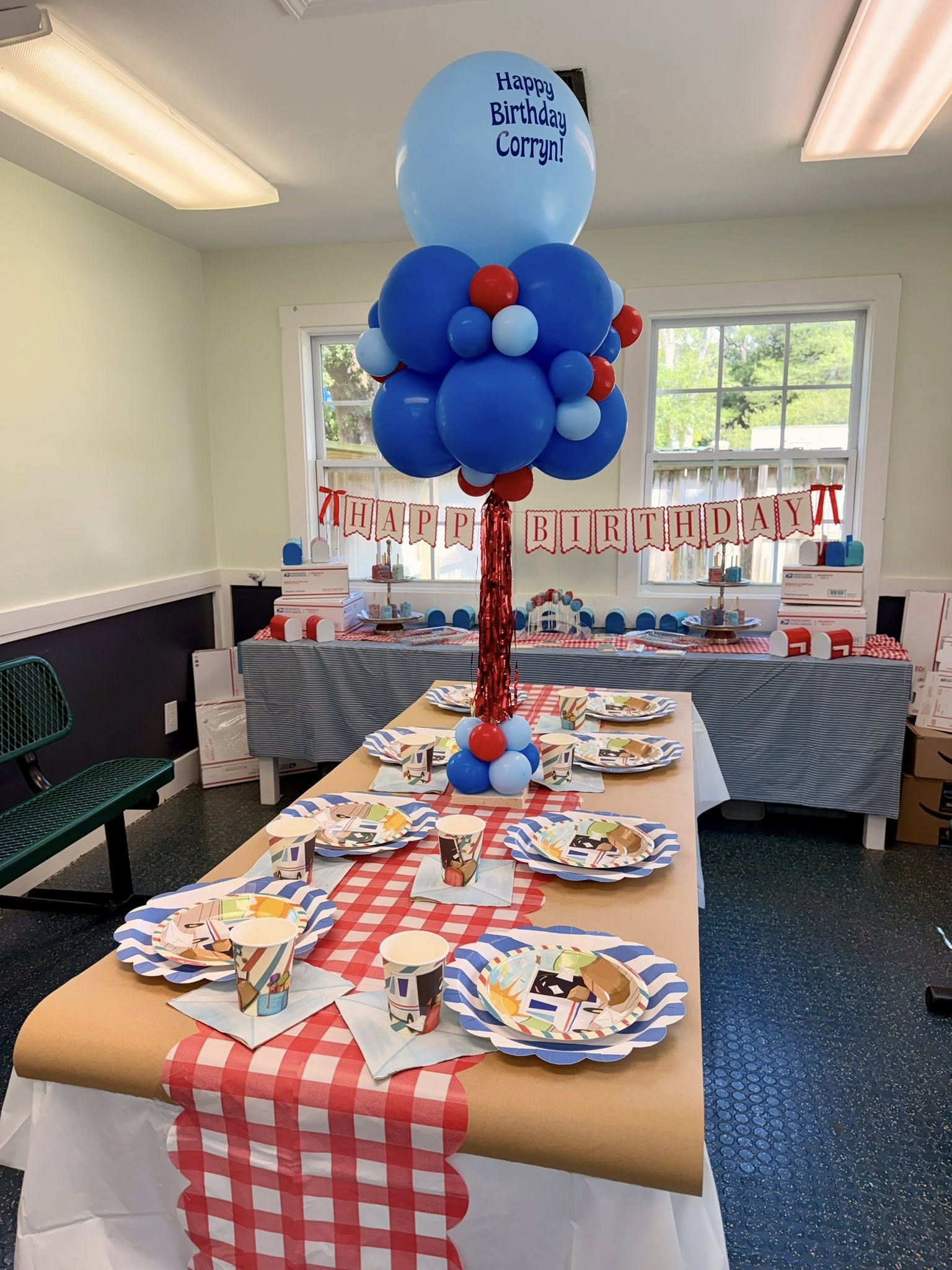 Birthday party table set for USPS-themed celebration with mail carrier plates, cups, and custom balloon centerpiece.