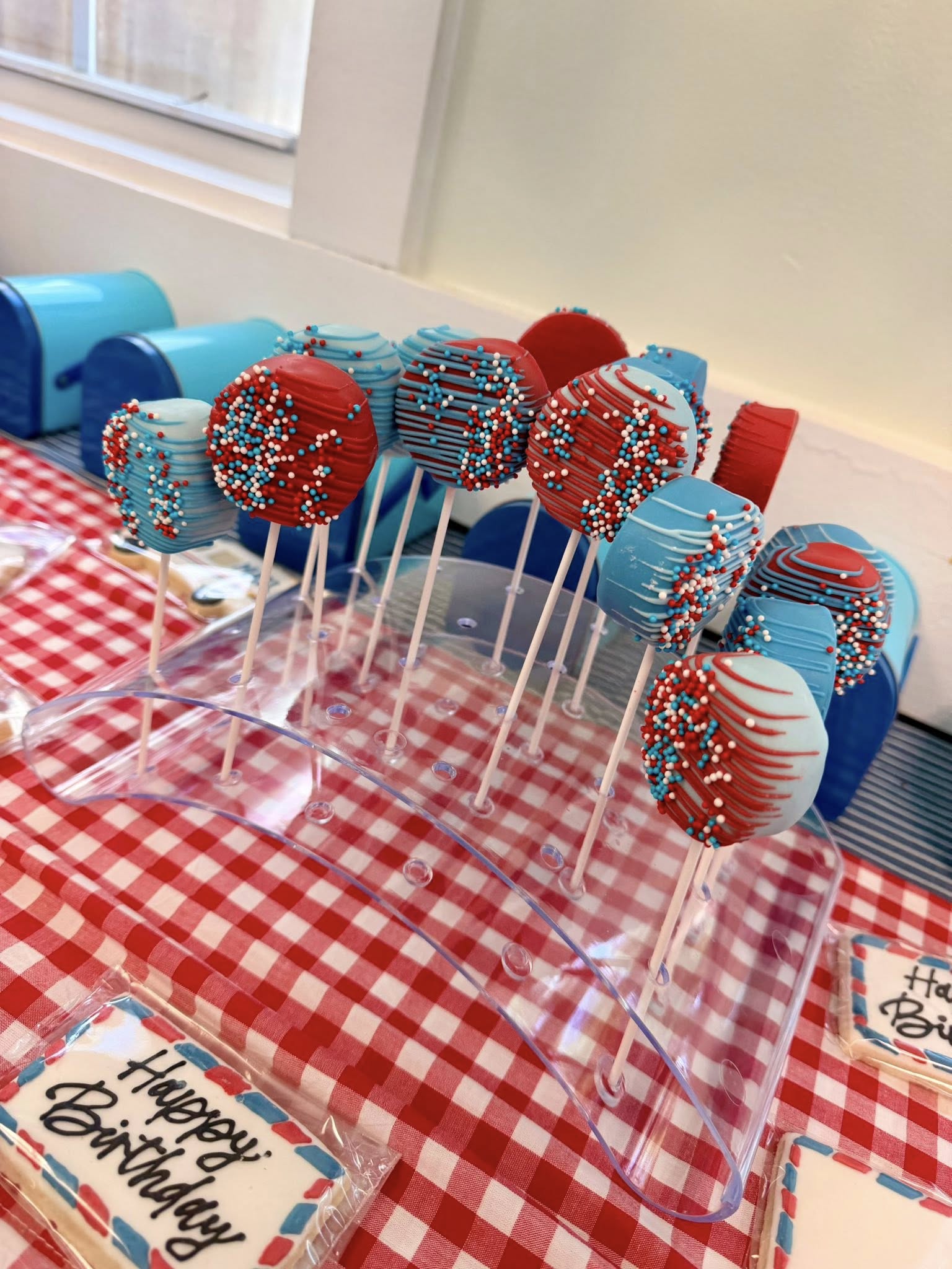 Red and blue chocolate-dipped cake pops with red and blue sprinkles on a display stand at a birthday party.