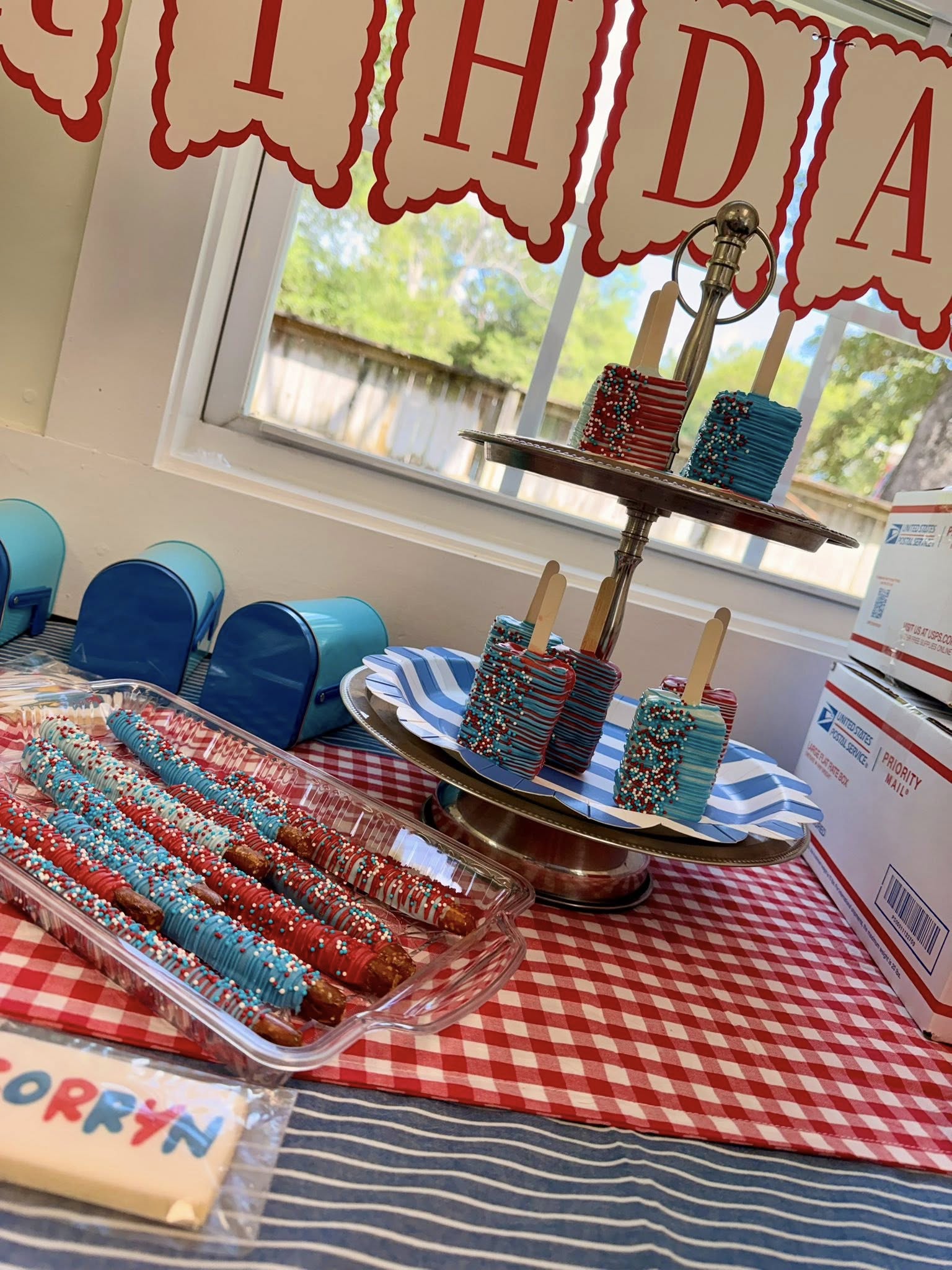 Table spread featuring red, white, and blue chocolate-covered pretzel rods and cake pops for a birthday party.