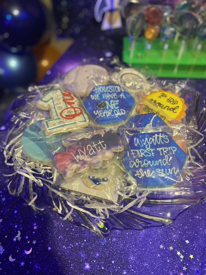 Space-themed first birthday party sugar cookies with personal name and birthday messages served in a glass bowl.