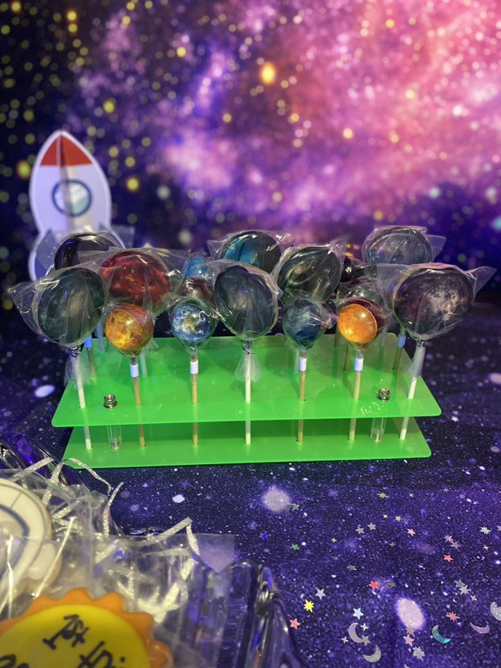 Set of planet-themed lollipops displayed on a green stand in front of a space-themed backdrop.