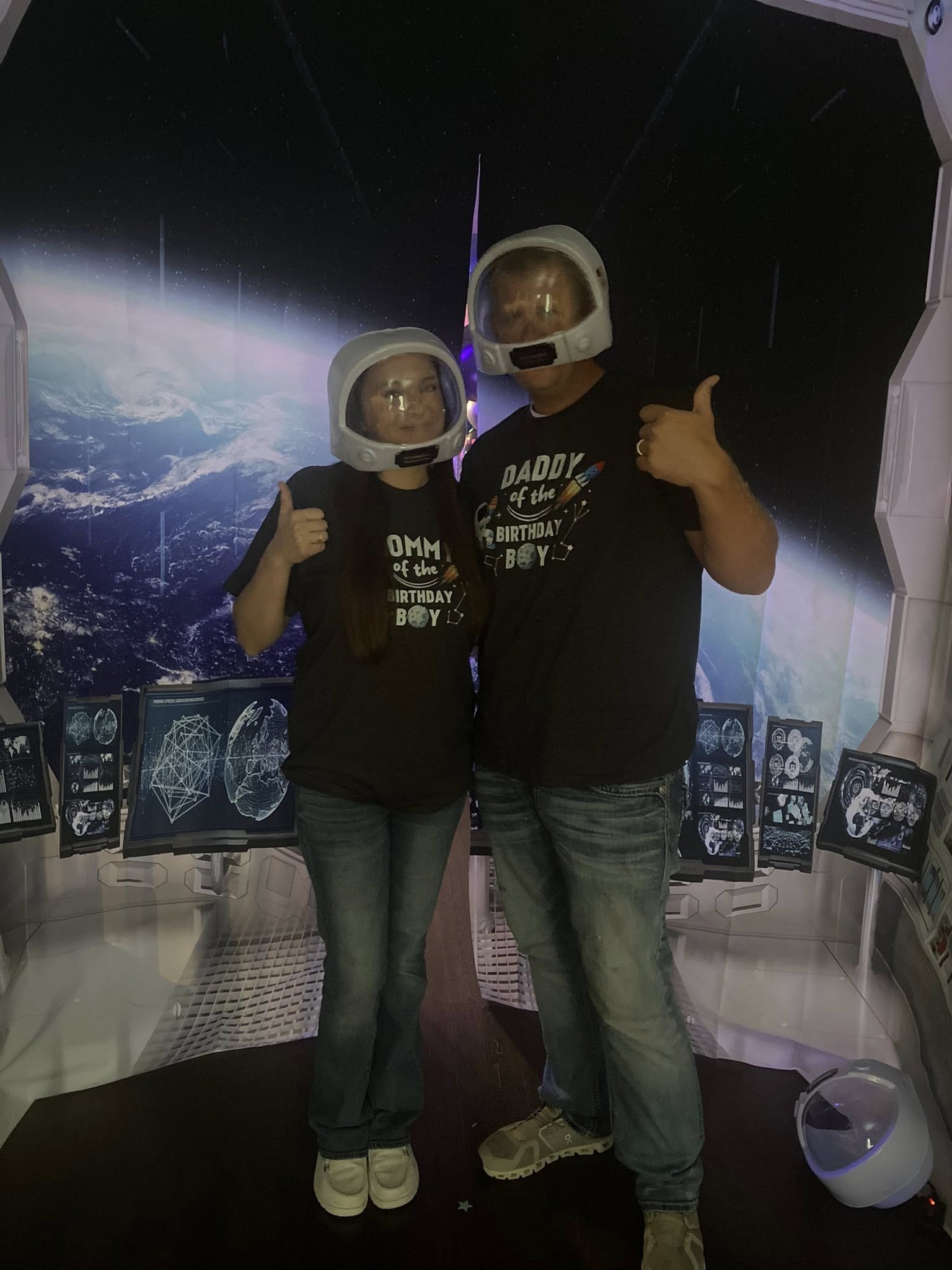Parents wearing astronaut helmets and matching birthday t-shirts in a space-themed backdrop.
