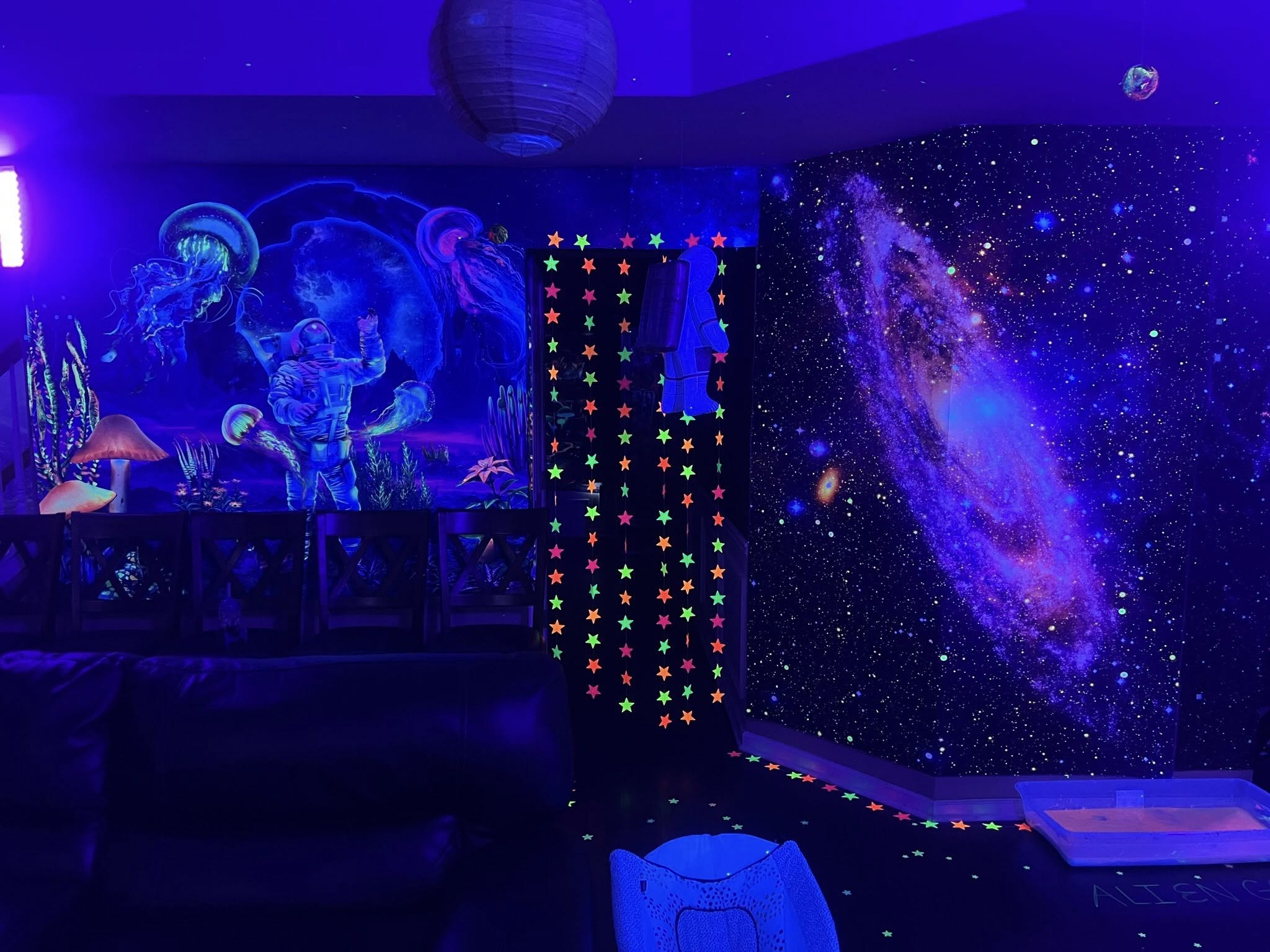 Room decorated with glow-in-the-dark space-themed wall murals, astronaut, galaxy, and hanging star garland.