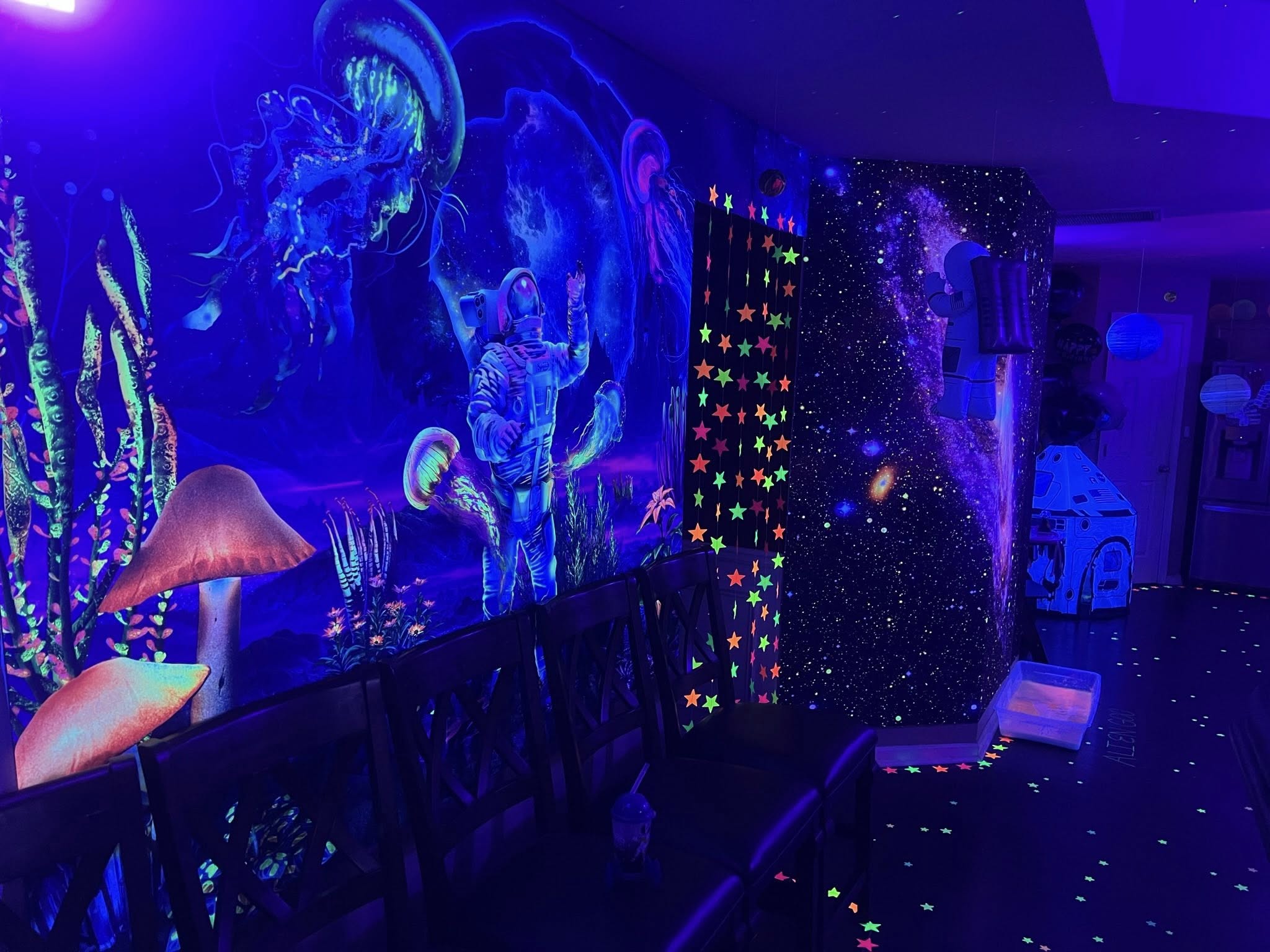 Room interior decorated with glowing neon space-themed wall murals featuring an astronaut and jellyfish.
