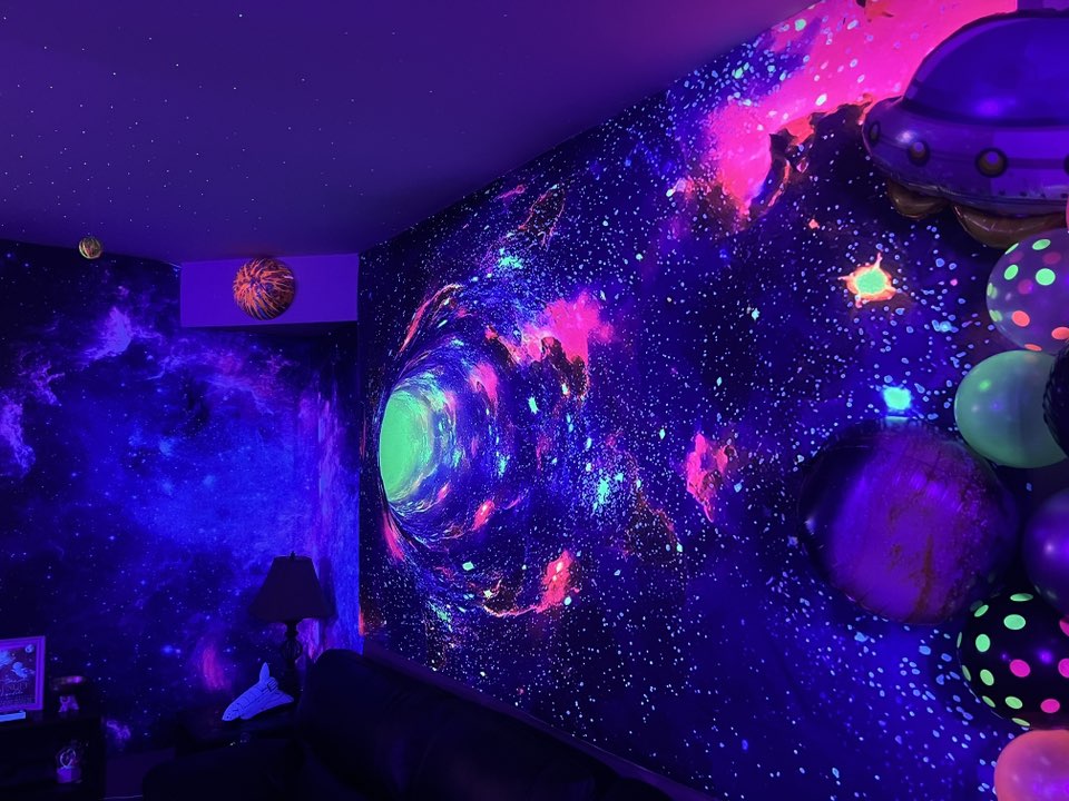 Room decorated with blacklight reactive galaxy mural featuring a glowing wormhole effect on the wall.