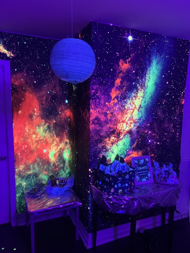 Space-themed party table set against a wall with a colorful neon galaxy mural