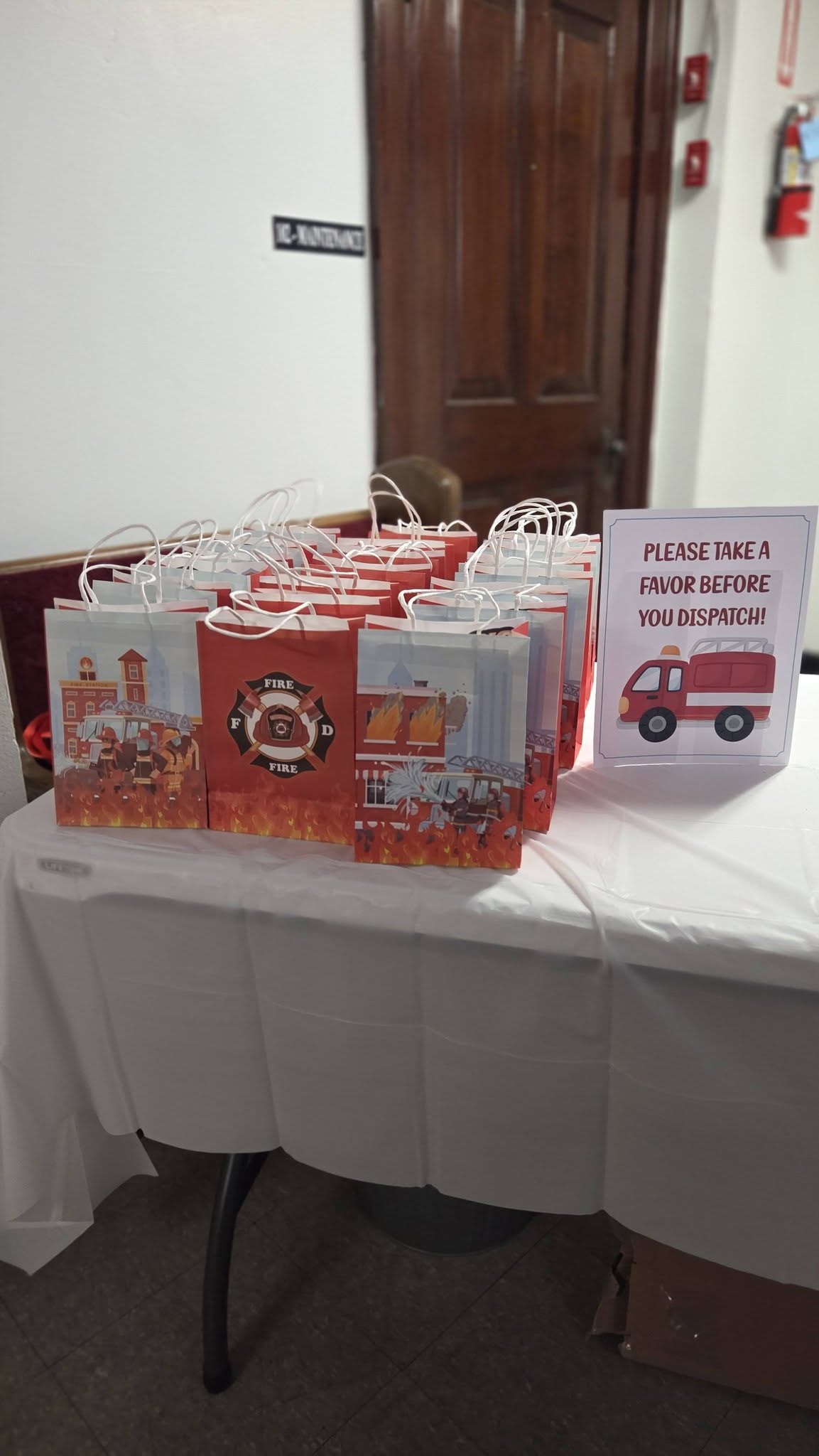 Table with fire-themed party favor bags and a sign reading Please take a favor before you dispatch.
