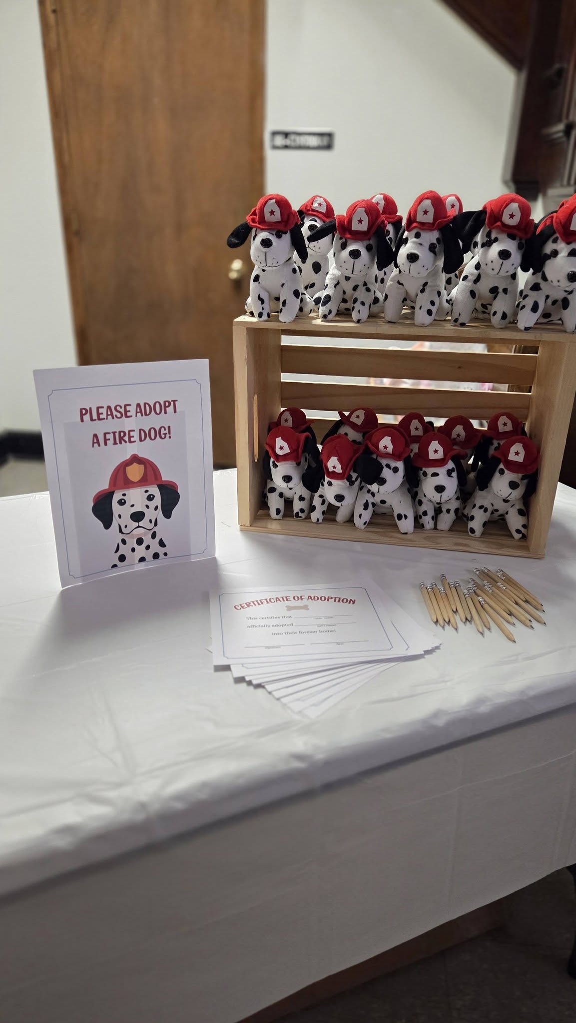 Plush dalmatian toys wearing firefighter hats on a wooden display with adoption certificates and pencils.