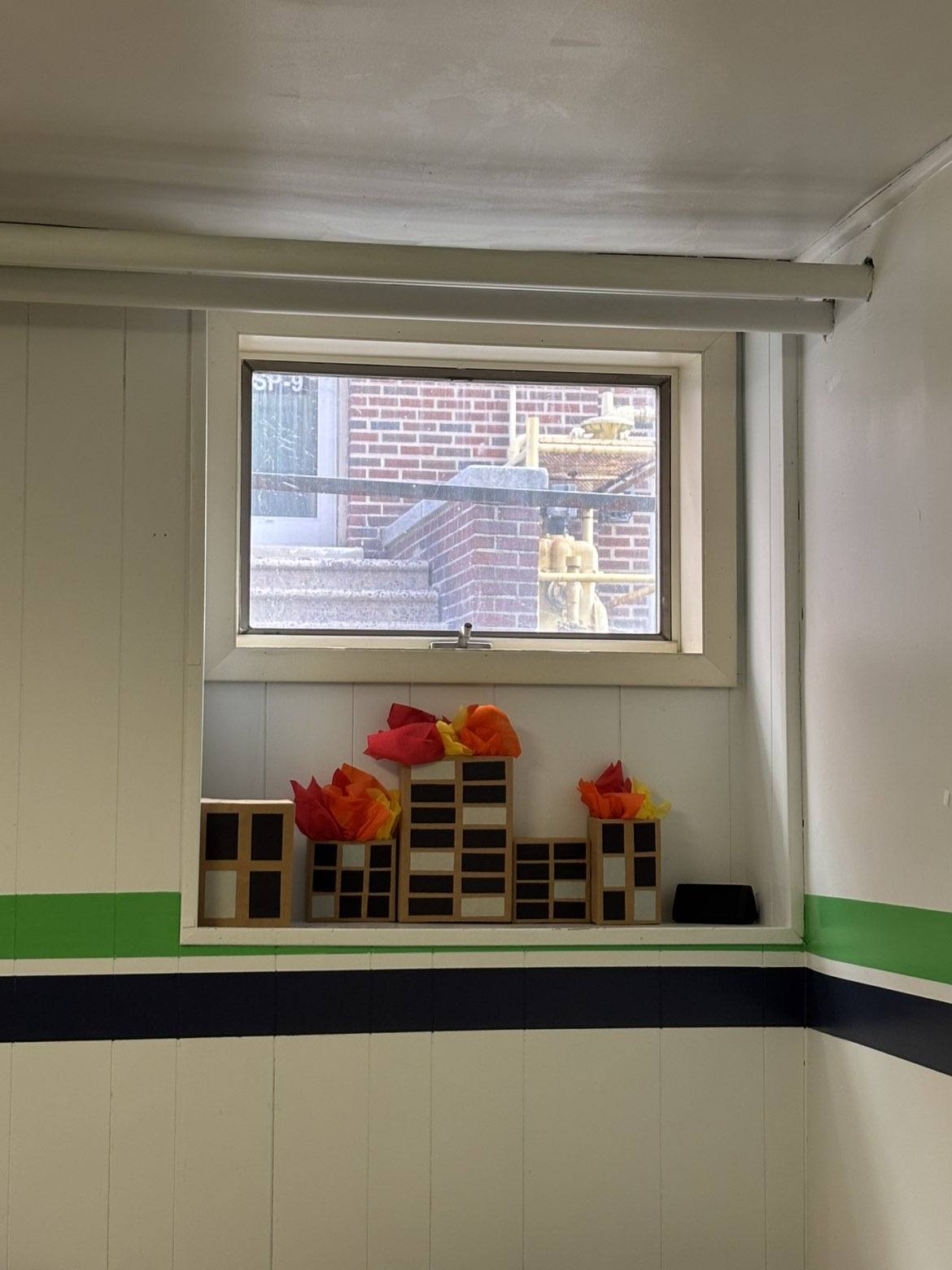 DIY cardboard building models with tissue paper flames displayed on a window sill.