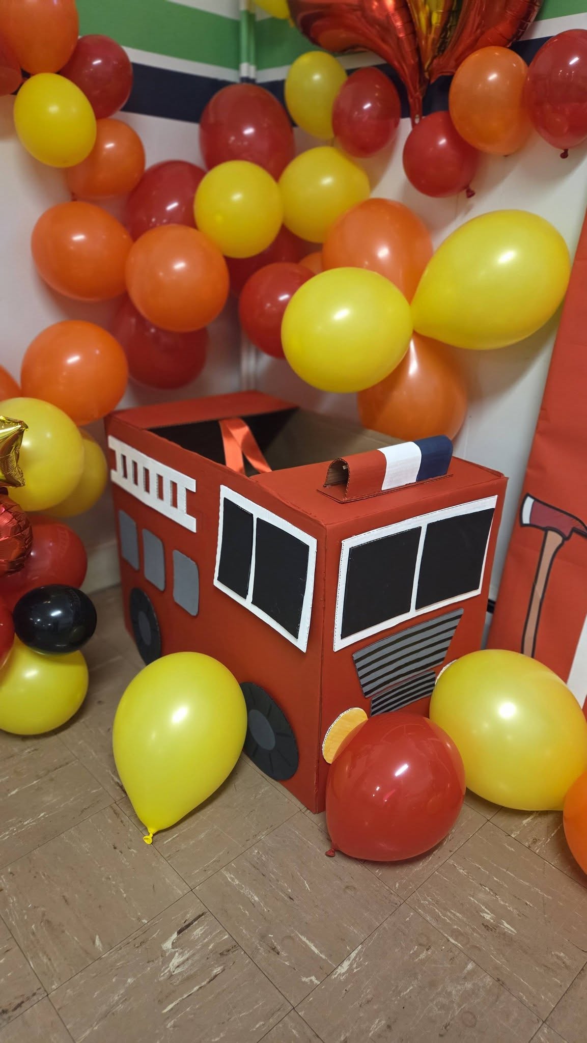Cardboard fire truck decorated as a party prop surrounded by red orange and yellow balloons