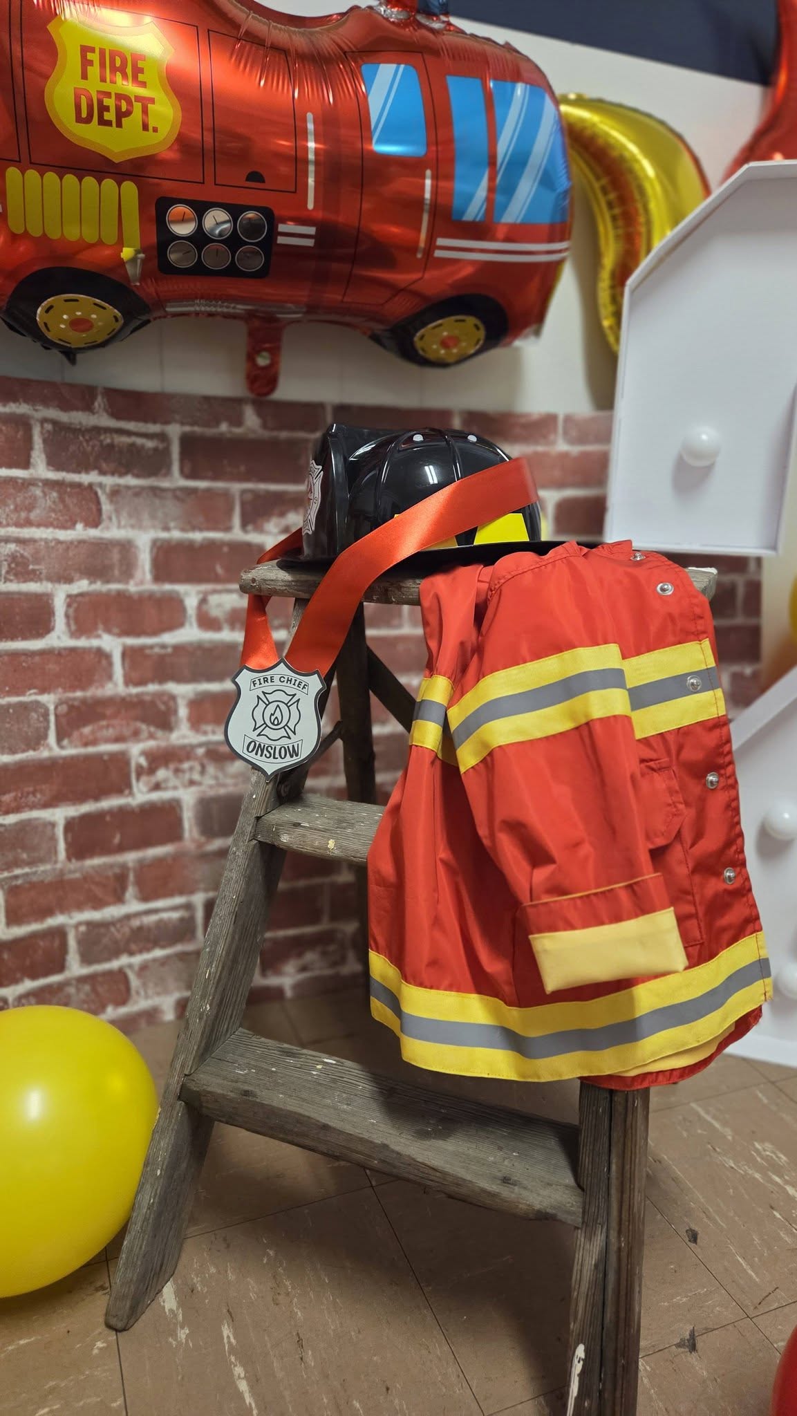 Child's firefighter costume with helmet and Fire Chief badge draped over a wooden step ladder.