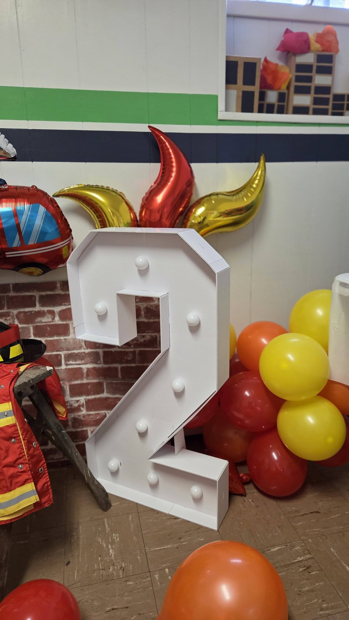 Large white marquee number 2 light decoration surrounded by red, yellow, and orange balloons for a second birthday.