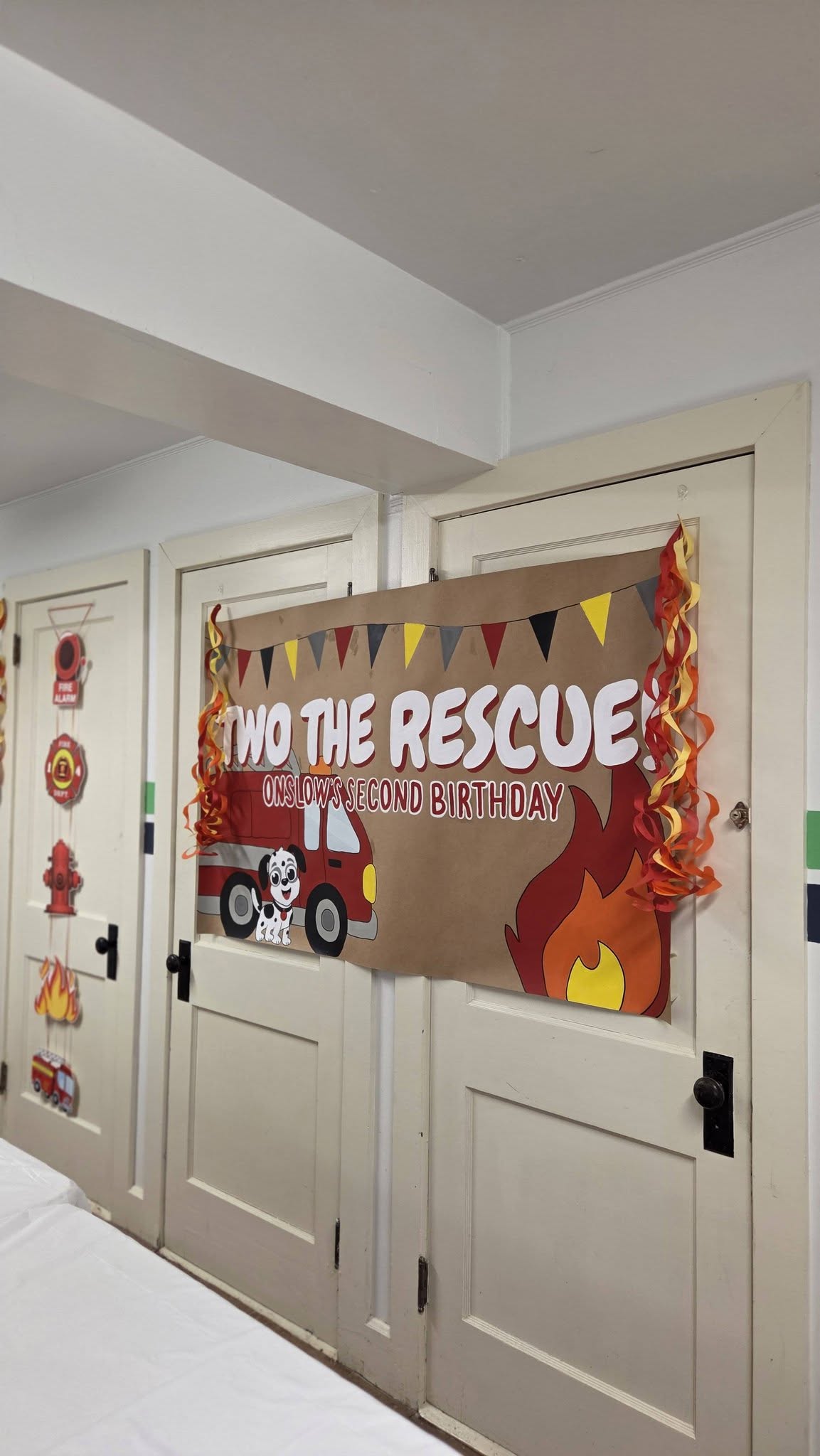 Firefighter-themed Two the Rescue banner for Onslow's second birthday hanging on a door with decor.